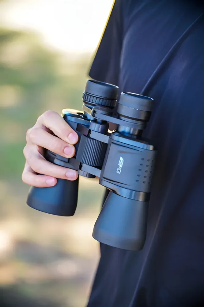 Persona sosteniendo binoculares Tasco 10x50 negros con diseño ergonómico, listos para su uso en observación al aire libre.