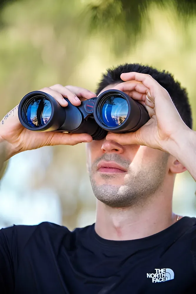 Persona utilizando binoculares Tasco 10x50 negros con lentes azulados durante una actividad de observación al aire libre.