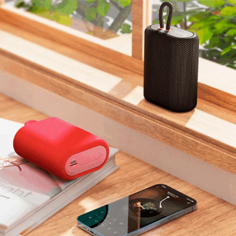 Parlante Bluetooth Hoco BS47 rojo y negro sobre escritorio, mostrando conexión inalámbrica con smartphone.